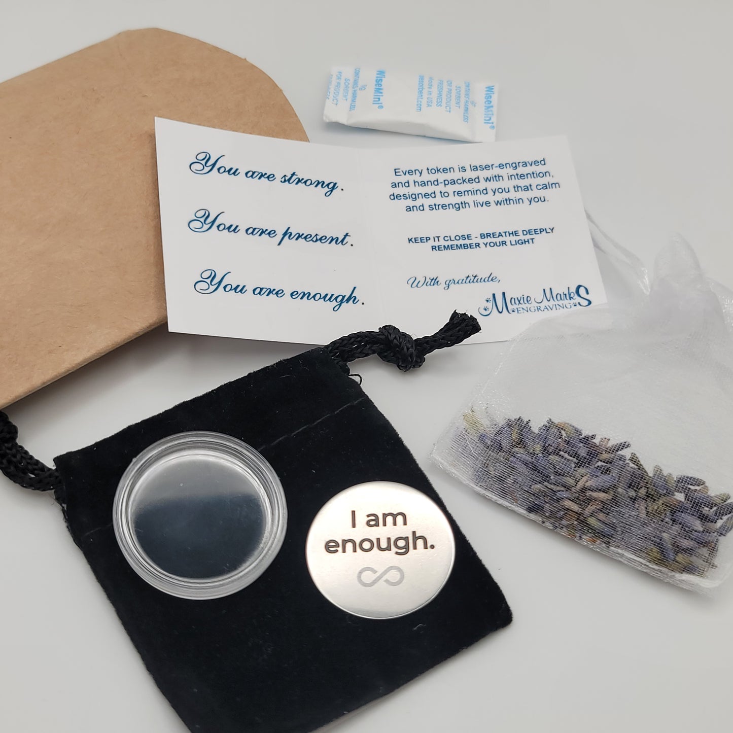 A complete display of the I Am Enough affirmation token set, including the engraved token, velvet pouch, acrylic capsule, lavender sachet, and affirmation card with the message “You are strong. You are present. You are enough.”