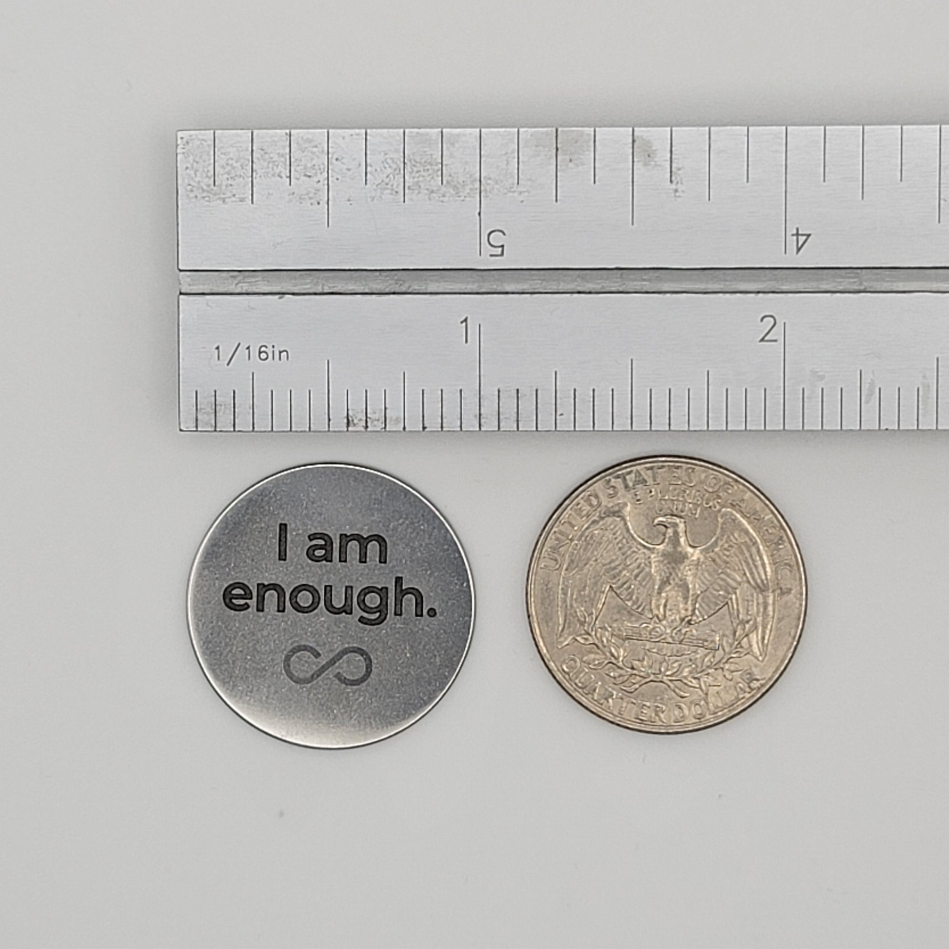 A stainless steel “I am enough” affirmation token shown beside a U.S. quarter and a ruler for size reference, illustrating the token’s compact and pocket-friendly dimensions.
